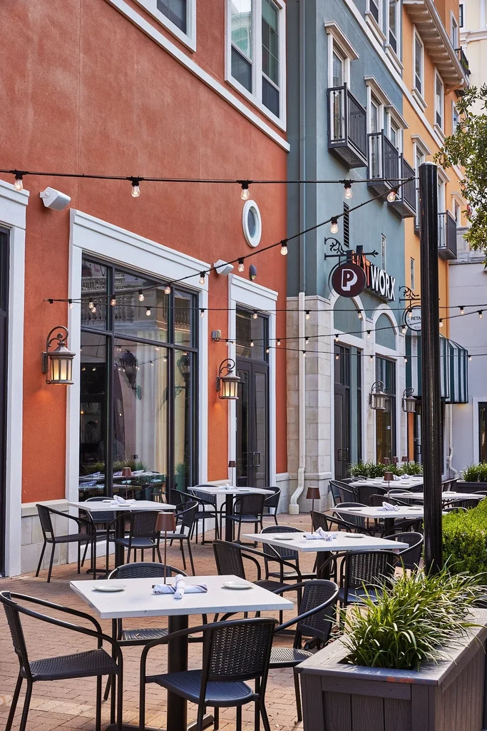 Outdoor restaurant patio with dining tables, string lights, colorful buildings.