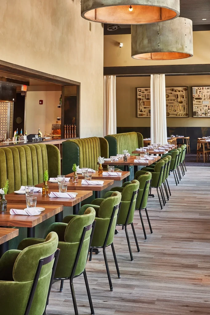 Modern restaurant interior with green velvet booths and antique utensil art.