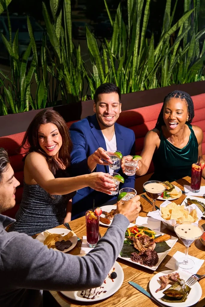 Four smiling people toast with shots and food at a restaurant.