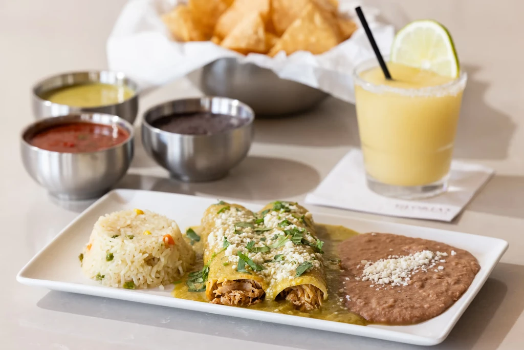 Plate of green chicken enchiladas, rice, beans, margarita, and dips.