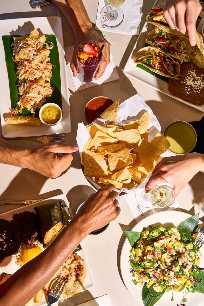 High-angle view of multiple hands sharing Latin American food and drinks.