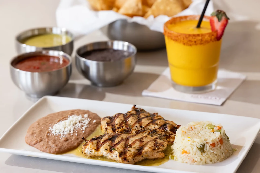 Restaurant plate of grilled chicken, beans, rice, with drink and sides.