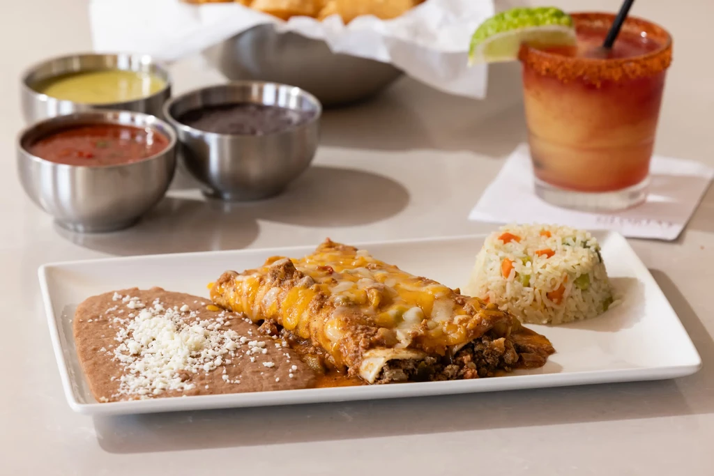 Mexican enchiladas plate with beans, rice, sauces, and a drink.