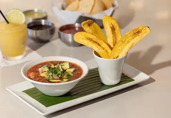 Garnished soup, fried plantains, and a yellow drink on a restaurant tray.