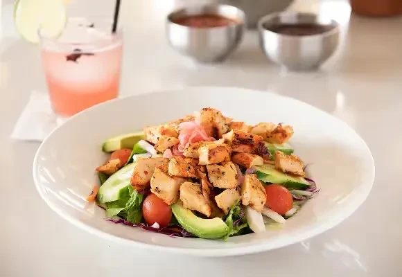 Chicken salad with grilled chicken, avocado, greens, and tomatoes.