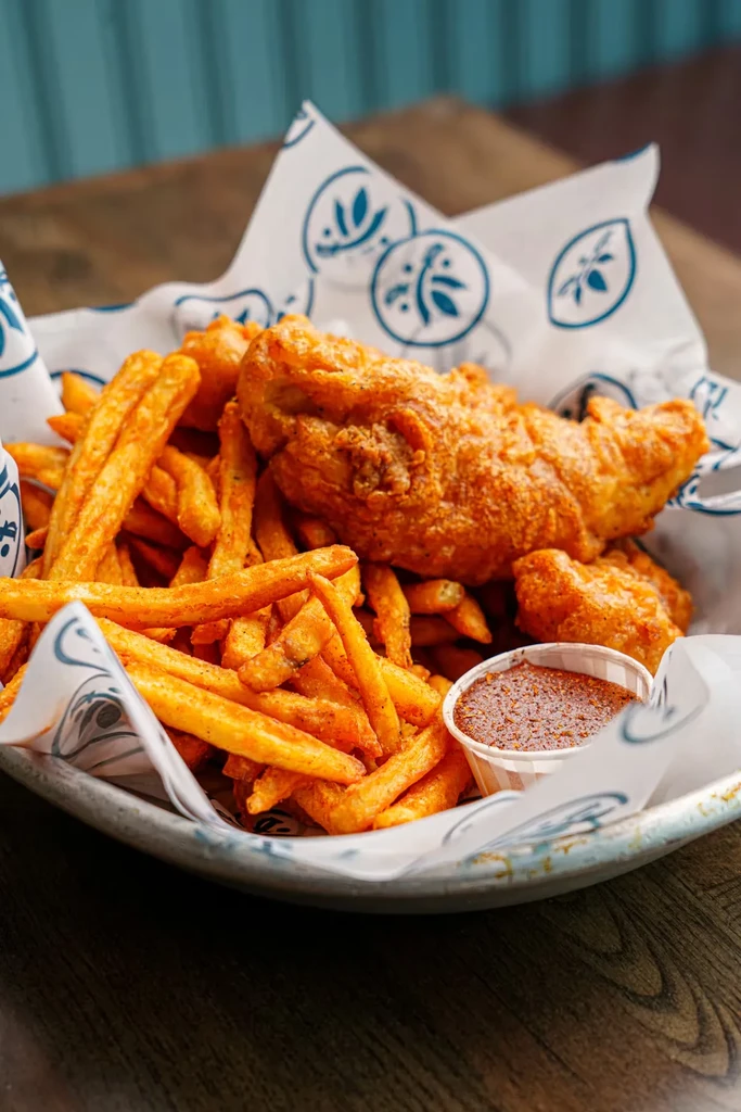 Fried food and seasoned fries in a basket with dipping sauce.