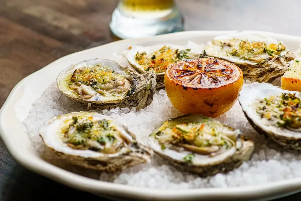 Six baked oysters with herb topping, grilled lemon, on ice.