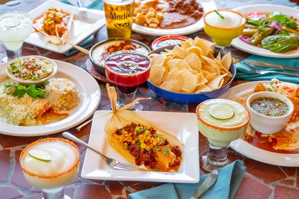 Vibrant overhead spread of Mexican food, margaritas, beer, and tamales.