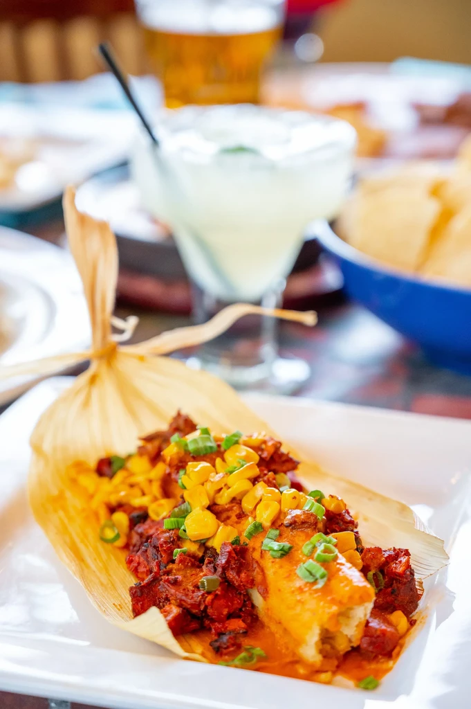 Close-up of unwrapped tamale with red filling, corn, and green onions.