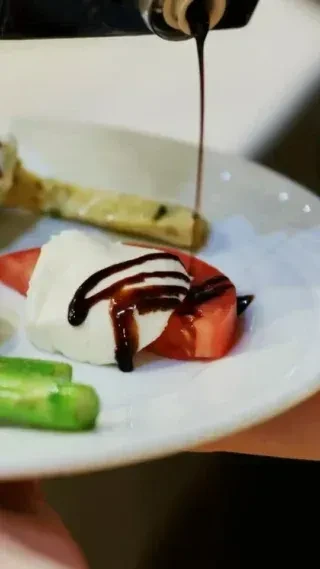 Close-up of balsamic glaze being drizzled on mozzarella and tomato.