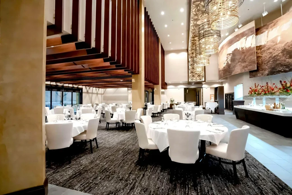 Spacious, empty restaurant dining room with set tables, buffet, chandeliers.