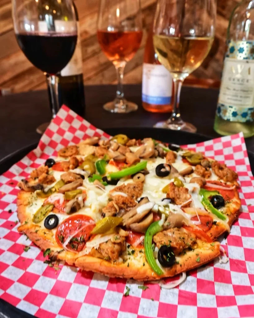 Close-up: generously topped pizza with pepperoni, vegetables, and wine.