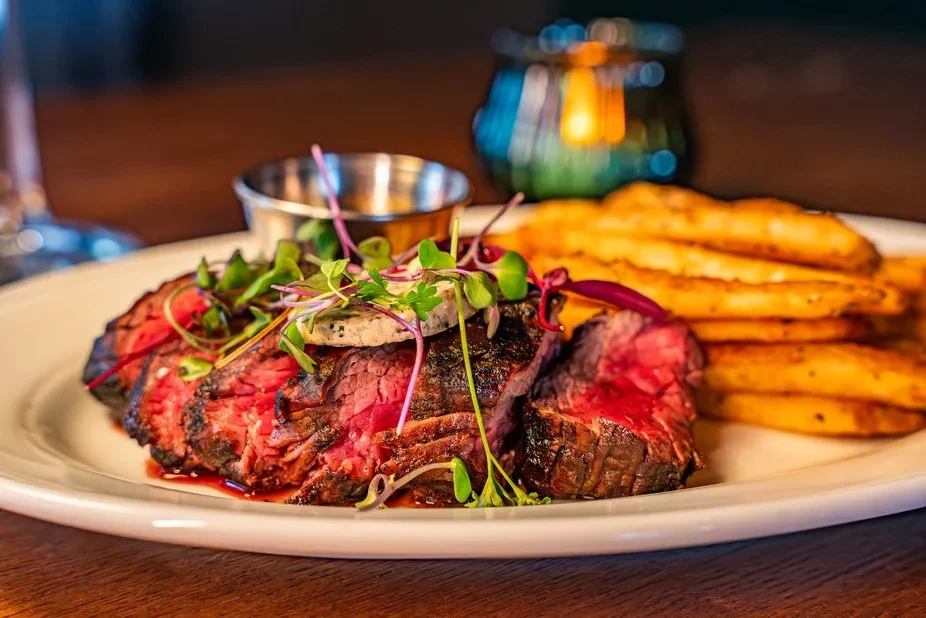 Plate of sliced medium-rare steak, fries, herb butter, microgreens.