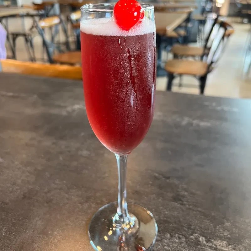 Chilled vibrant red cocktail with foam and cherry in a flute.