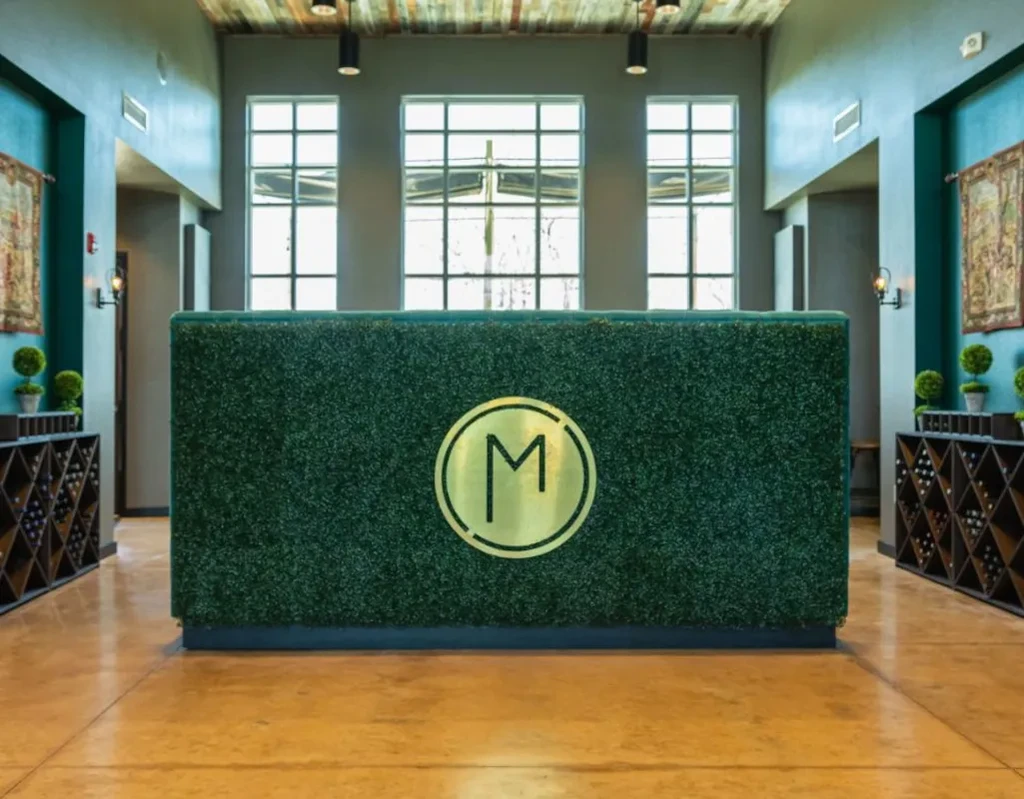 Modern reception with grass-covered counter and golden 'M' emblem.