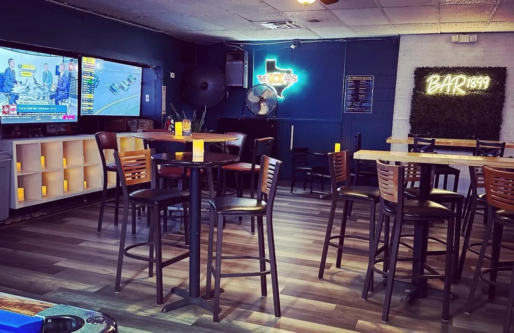 Modern bar interior with TVs, neon signs, high-top tables, and pool.