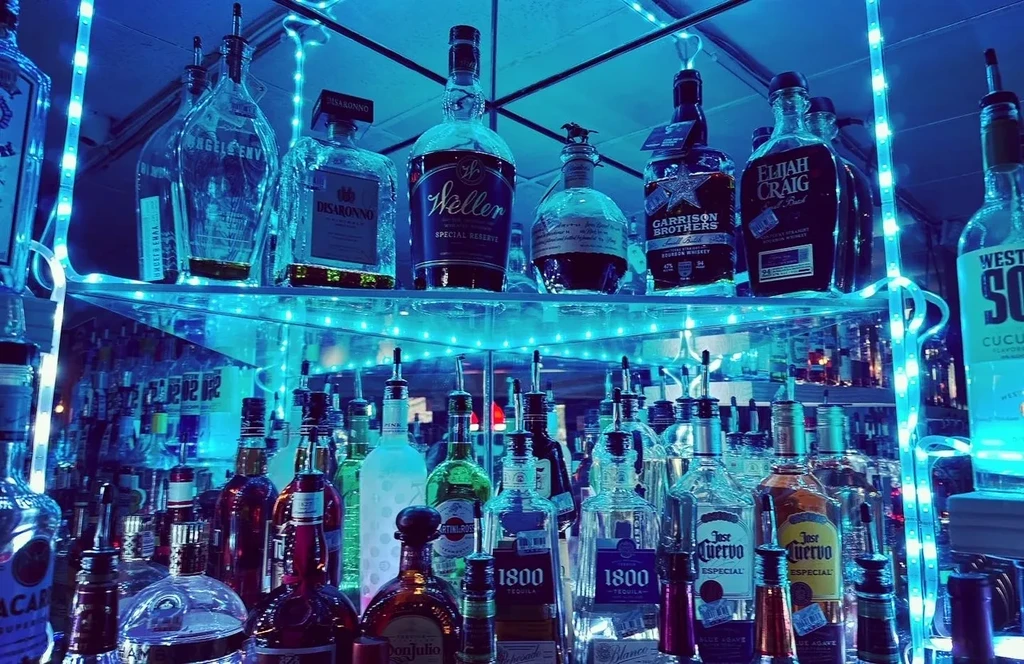 Well-stocked bar shelves brightly lit with blue LED lights.