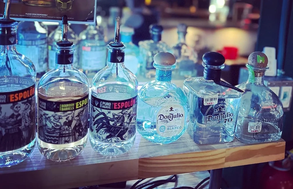 Close-up of Espolón, Don Julio, and Patrón tequila bottles on a bar.