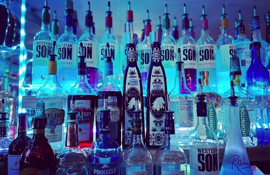 Bar shelf with many liquor bottles, pourers, and blue LED lights.