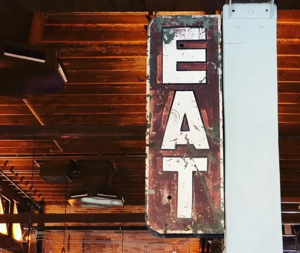 Vertical distressed 'EAT' sign with chipped white letters on rusty background.