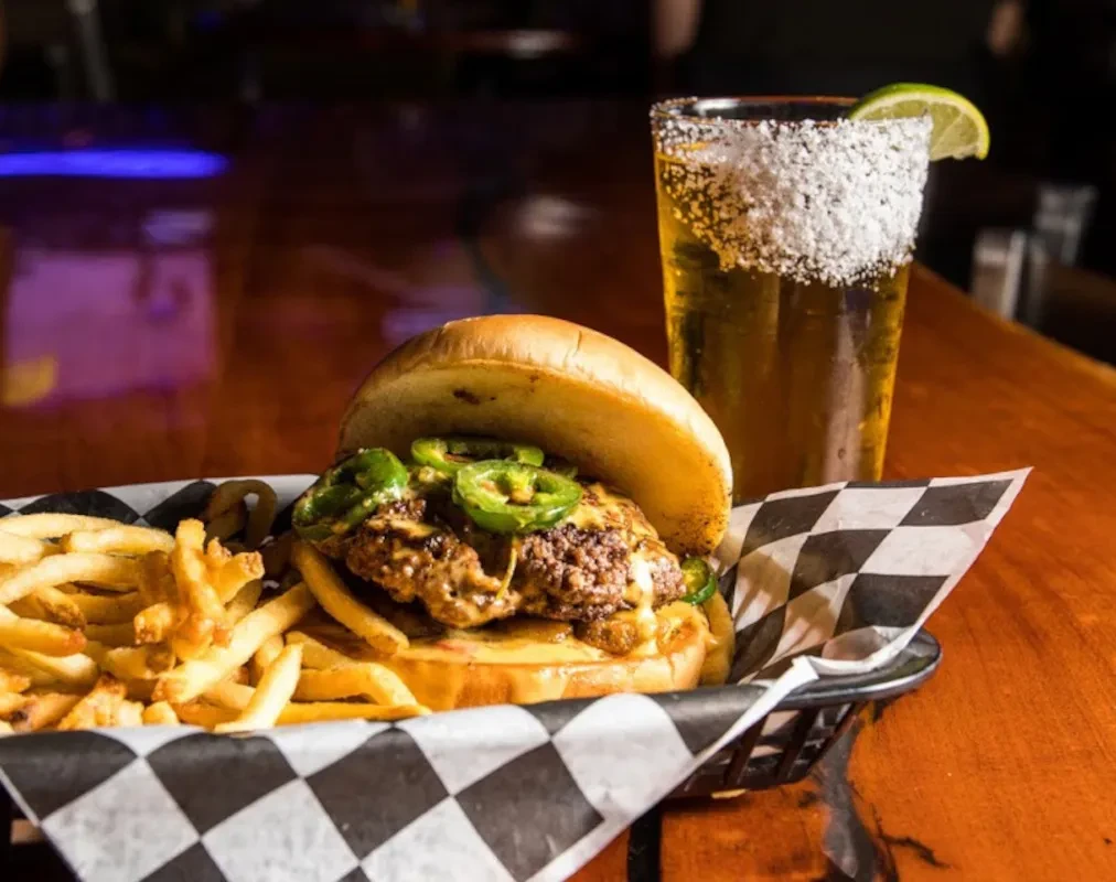 Gourmet burger with jalapeños, fries, and amber drink with lime.