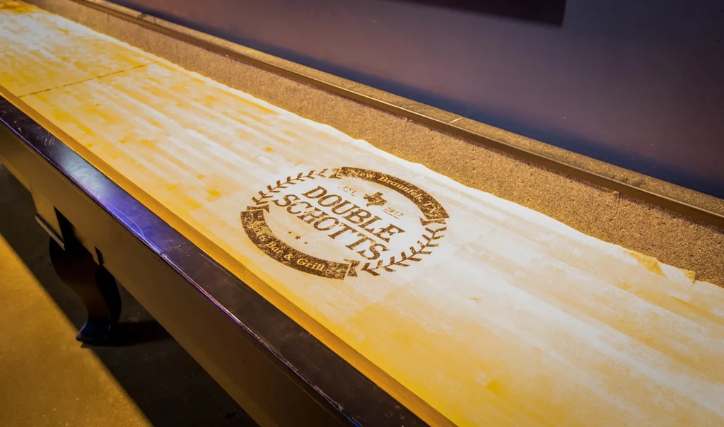 Close-up of a wooden shuffleboard table featuring the DOUBLE SCHOTTS logo.