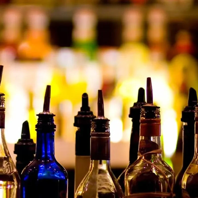 Various liquor bottles with pour spouts against a warm, blurred bar background.