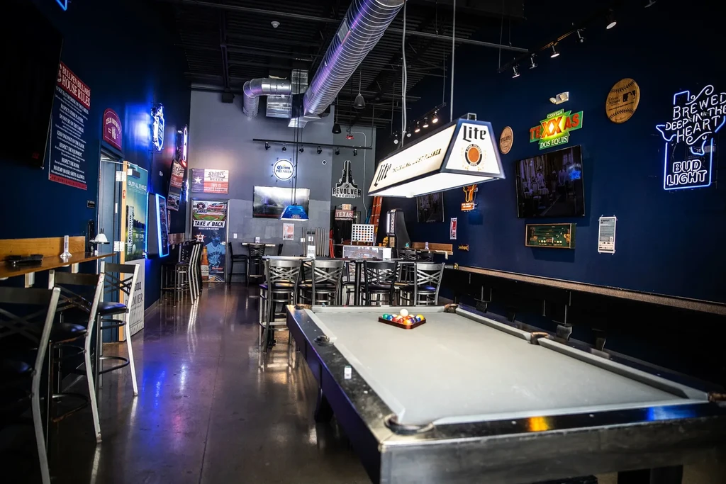Dark sports bar with pool table, TVs, and bright neon signs.