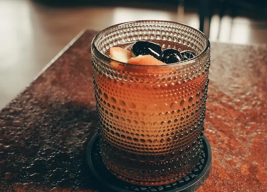 Amber beverage in a textured glass with fruit and dark pearls.