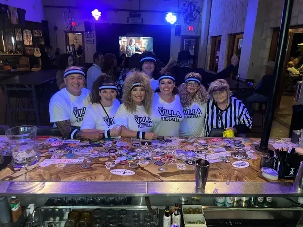 Kickball team and referee pose behind a sticker-covered bar.