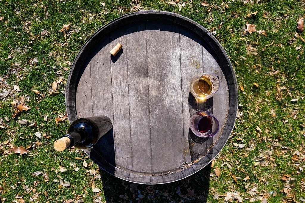 Weathered wine barrel outdoors with bottle, corks, and two wine glasses.