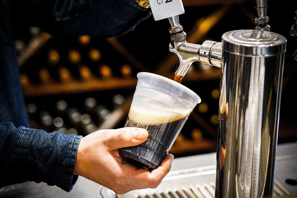 Hand holds cup filling with dark, foamy beverage from a tap.