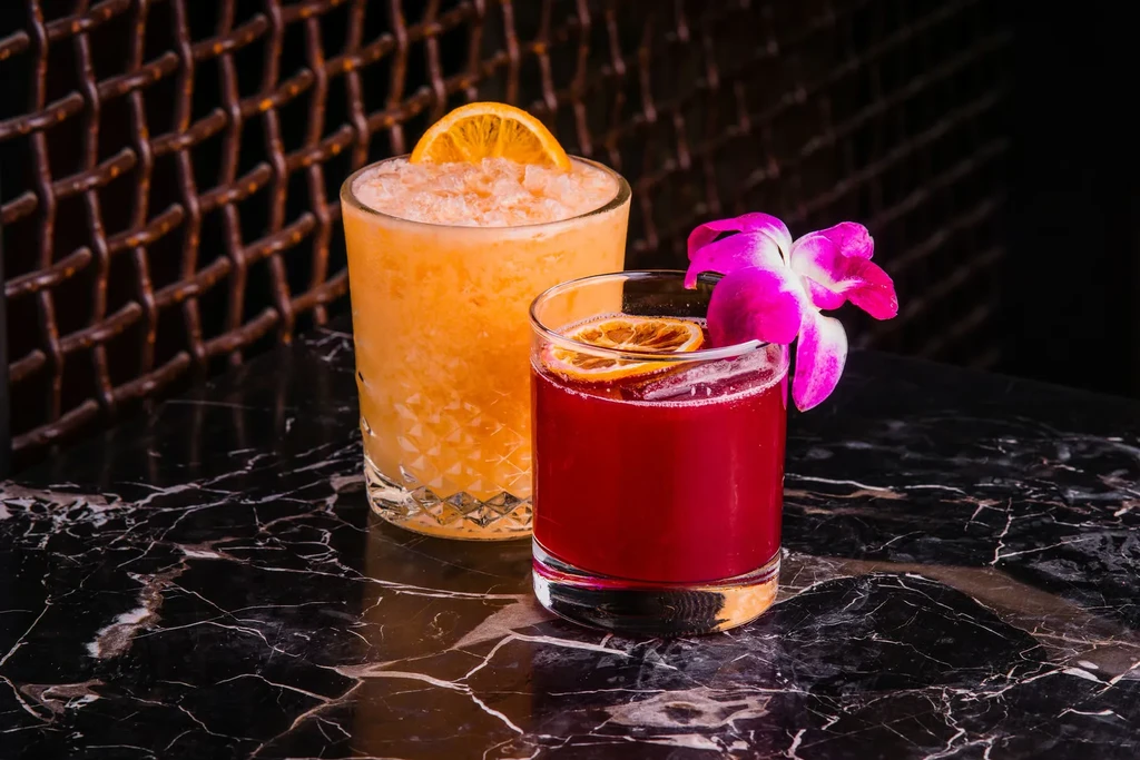 Orange and red cocktails with garnishes on dark, reflective surface.