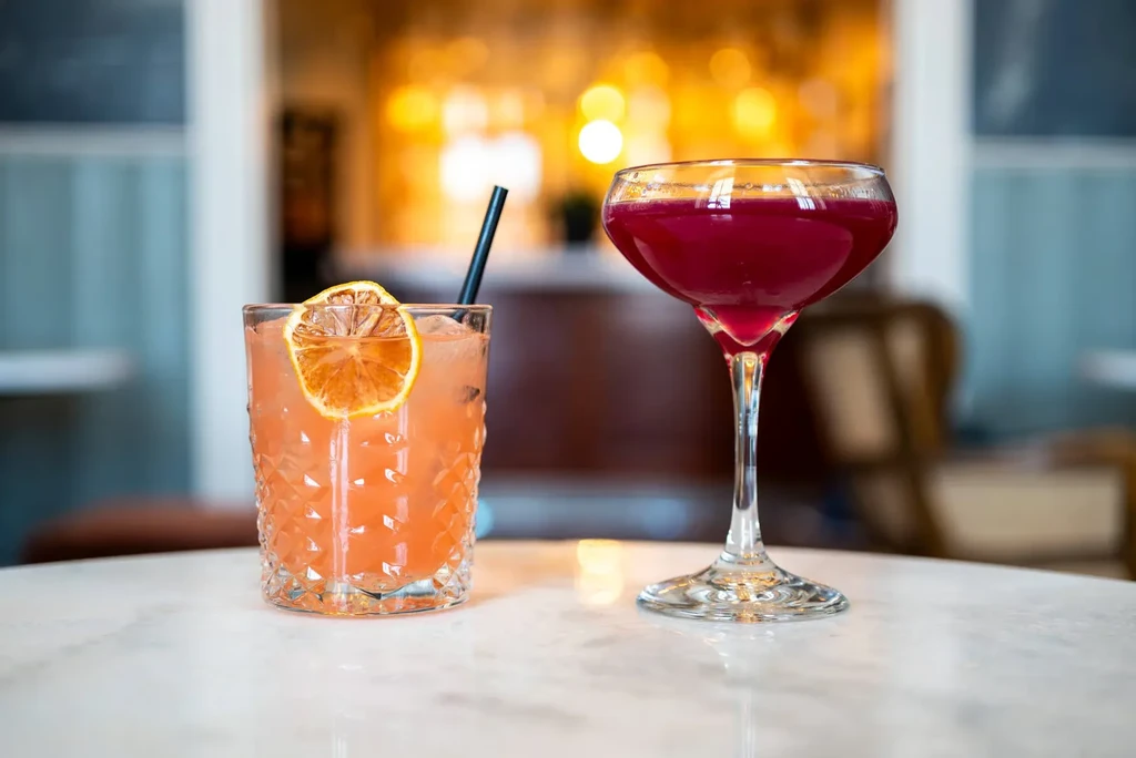 Two cocktails: one orange in a lowball, one red in a coupe.