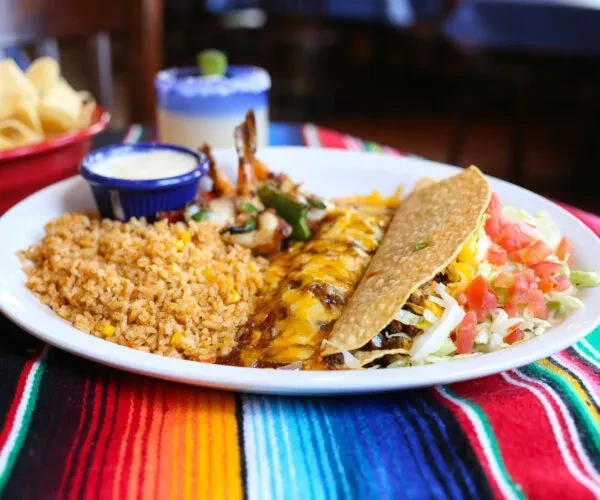Tex-Mex combo plate with rice, taco, enchilada, shrimp, on serape.