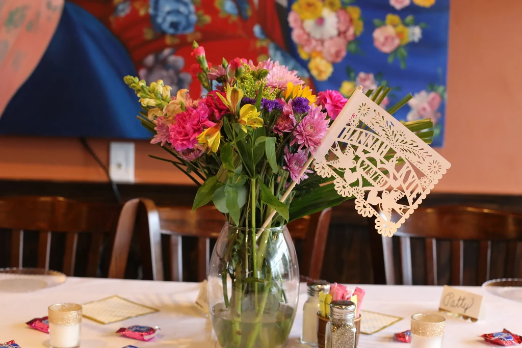 Restaurant table with colorful flowers and 'Hannah & Kyle' wedding date flag.