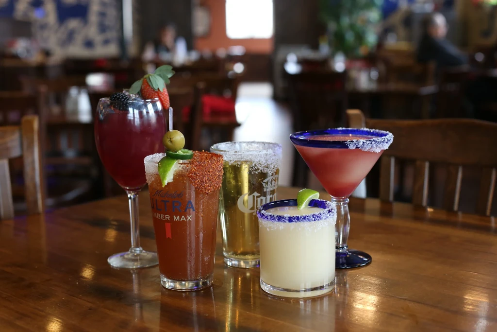 Five diverse alcoholic drinks on a wooden table in a restaurant.