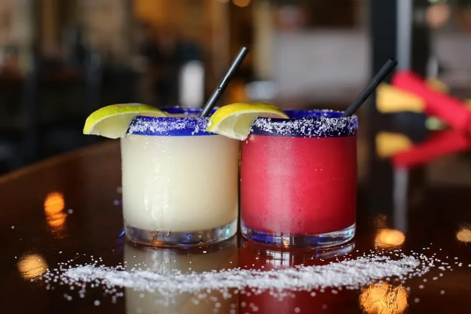 Yellow and pink margaritas with blue rims, salt, lime, and straws.