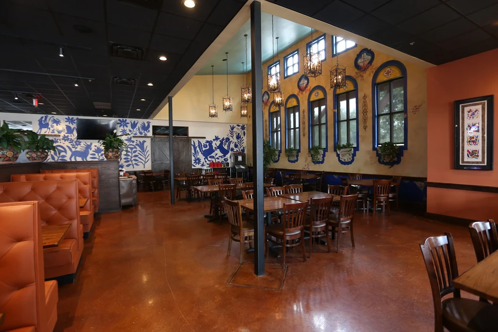 Empty rustic restaurant with orange booths and a blue folk art mural.