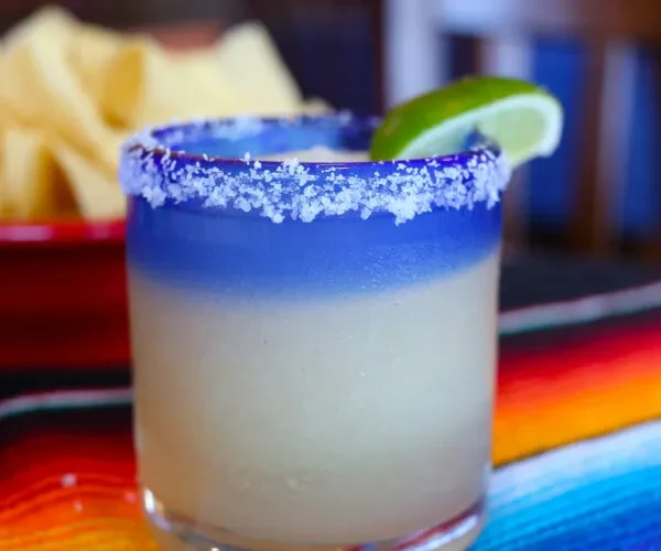 Salt-rimmed frozen margarita with a lime wedge on a serape.