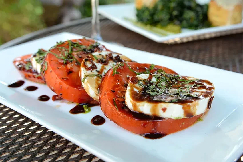 Three Caprese slices with mozzarella, balsamic glaze, and herbs.