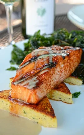 Grilled salmon with creamy sauce, polenta, and green vegetables.