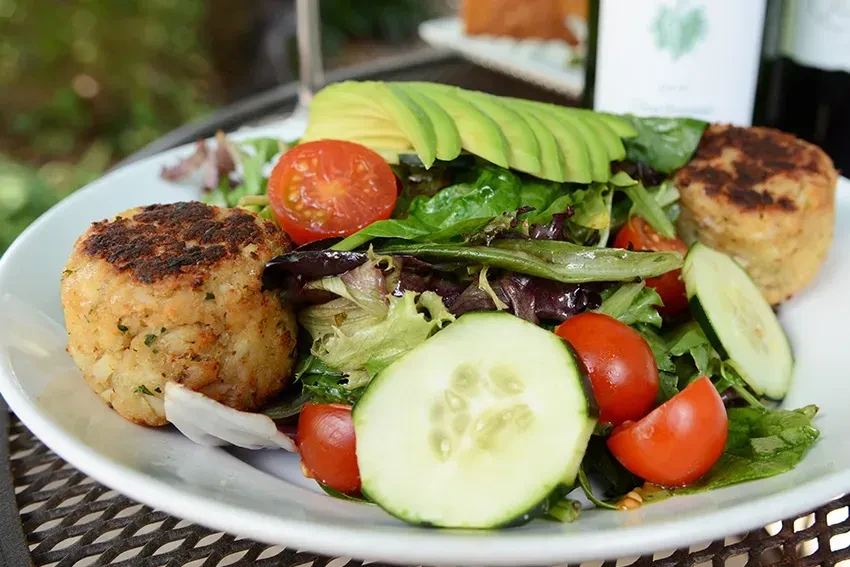 Gourmet salad with two golden crab cakes, mixed greens, avocado, and tomatoes.