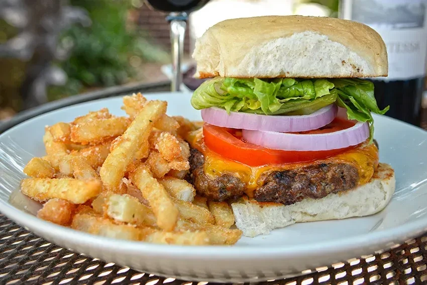 Cheeseburger with melted cheese, tomato, onion, lettuce, and crispy french fries.