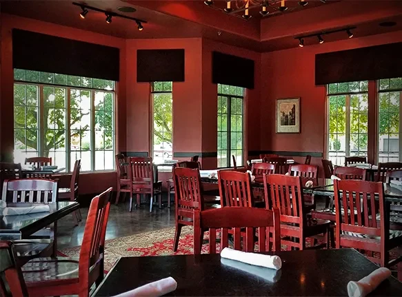 Empty restaurant dining room with red walls and dark wood tables.