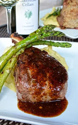 Steak, dark sauce, mashed potatoes, asparagus on a white plate.