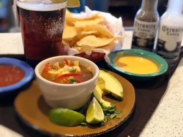 Tortilla soup with avocado, lime, chips, queso, salsa, and drinks.