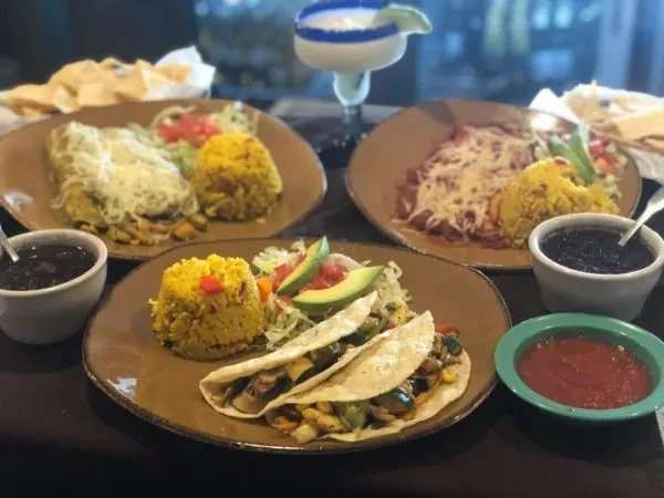 Mexican food plates: tacos, enchiladas, rice, beans, and a margarita.
