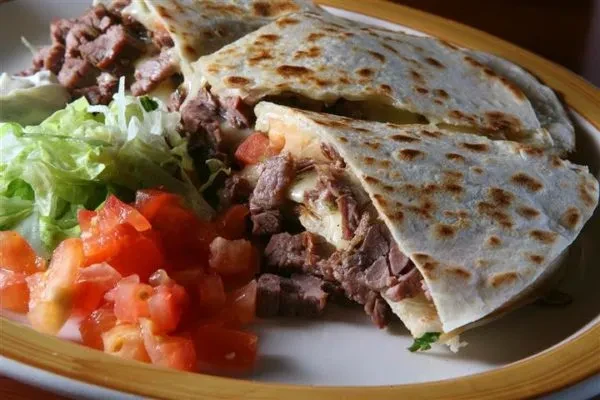 Cut steak and cheese quesadilla with lettuce, tomato, and sour cream.