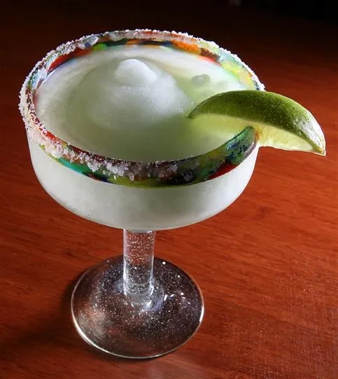 Frozen pale green margarita, colorful crystal rim, lime wedge.